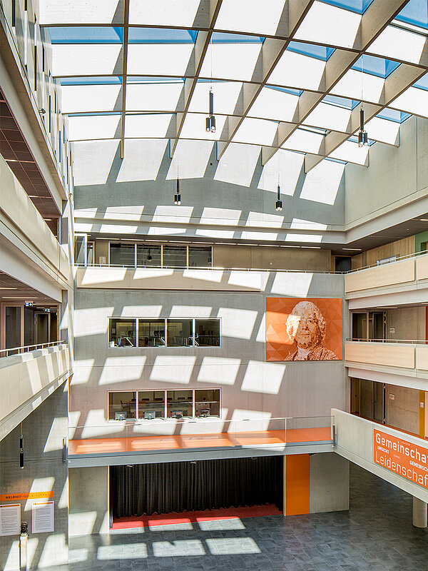 Innenansicht des Willibald-Gluck-Gymnasiums in Neumarkt mit großem Glasdach von LAMILUX, das den Raum mit Tageslicht durchflutet.