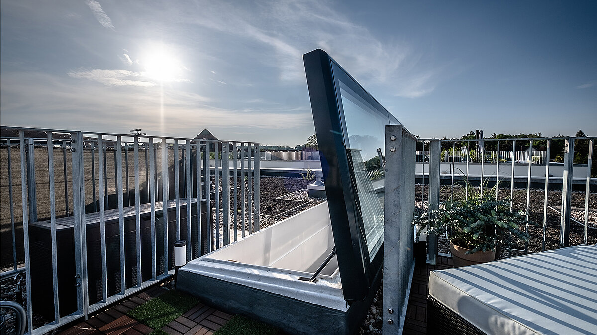 Flachdach Ausstieg bei einem Townhouse in Berlin mit moderner Glasabdeckung und Geländer, Sonnenschein im Hintergrund.