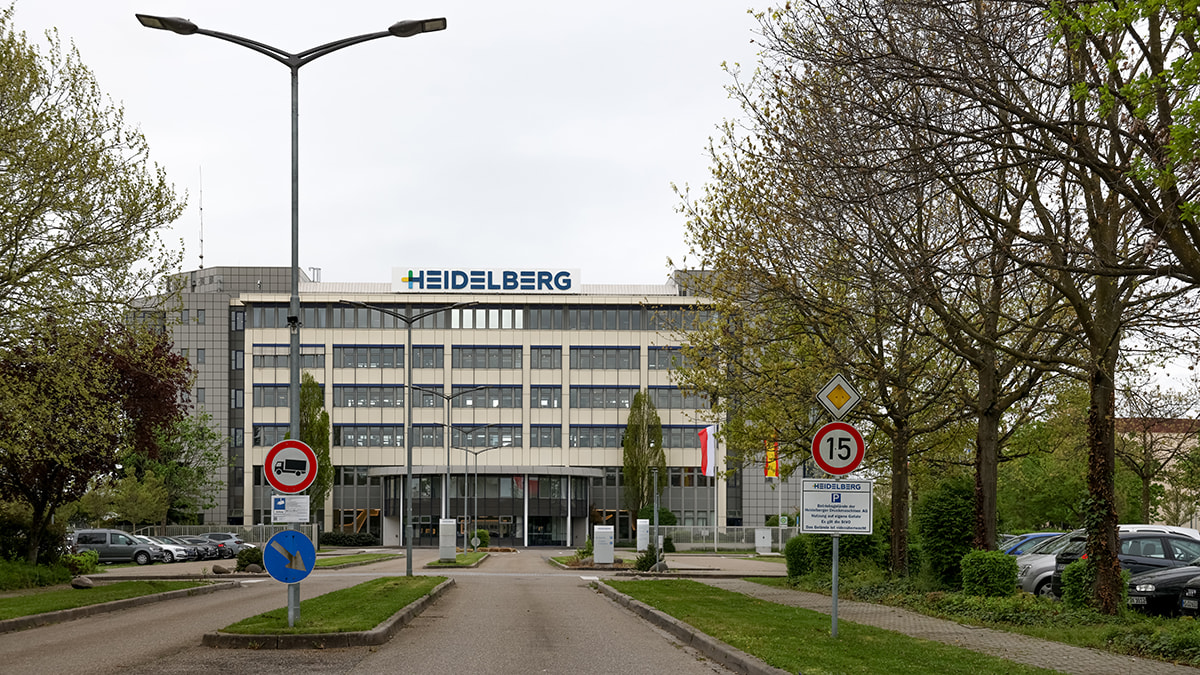 Außenansicht des Heidelberger Druckmaschinen Gebäudes mit Bäumen und Parkplätzen.